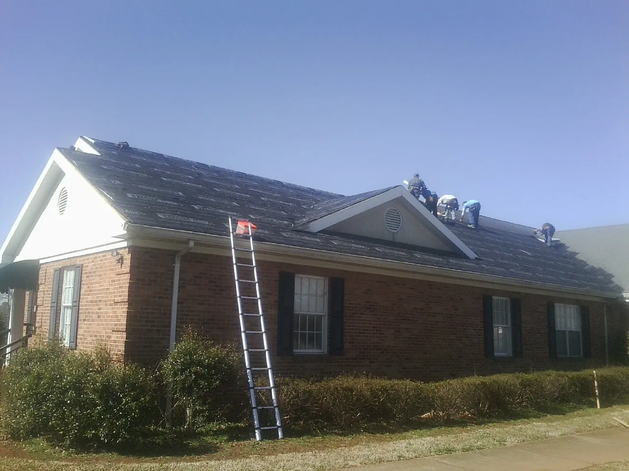 Crew tearing shingles off a brick ranch roof with a ladder set — Metal Roof Repair work by our crew in Montchanin