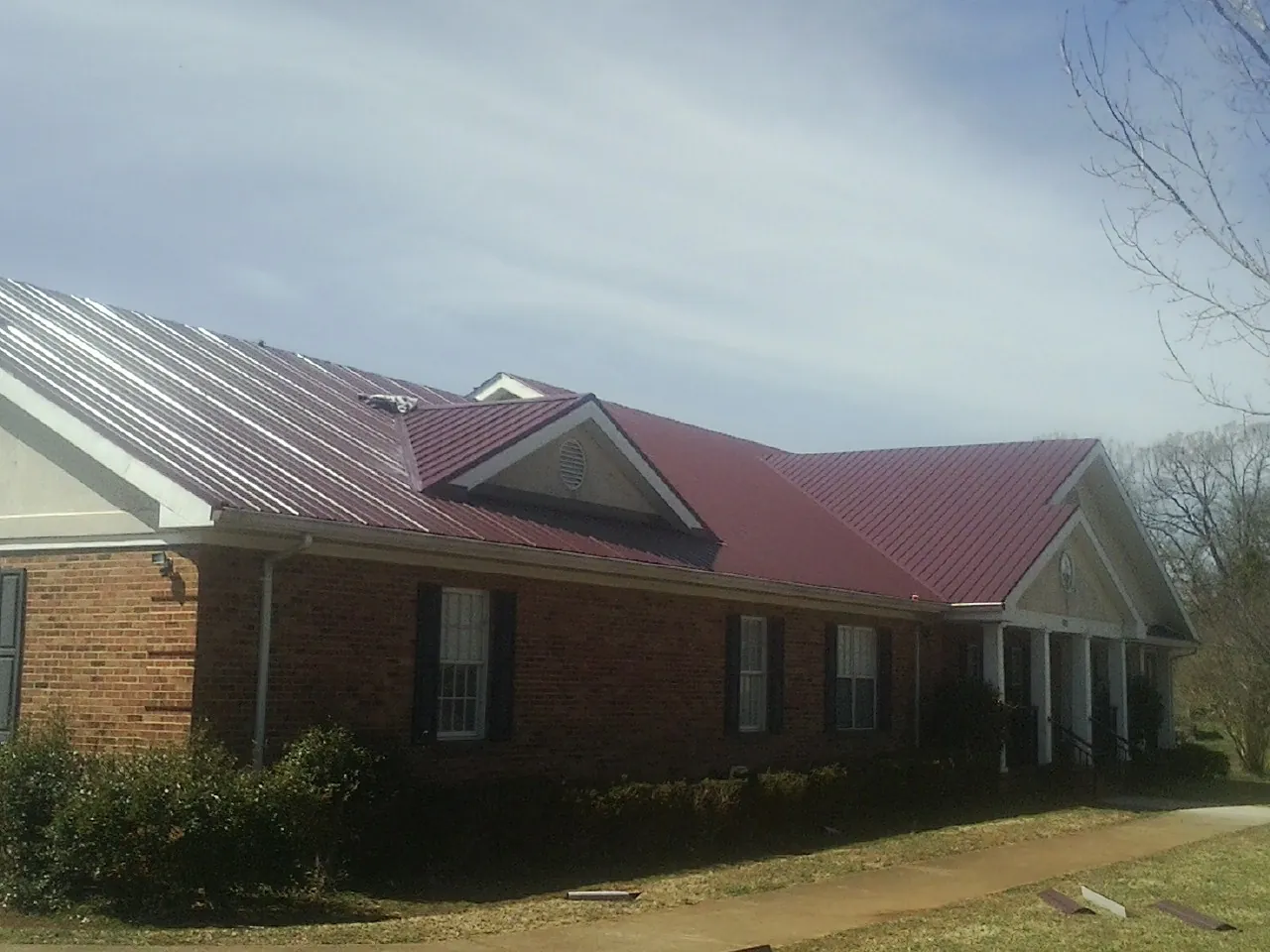 Red metal roof with gabled entries on a long brick building, from a Hail Damage Roof Repair job in Montchanin