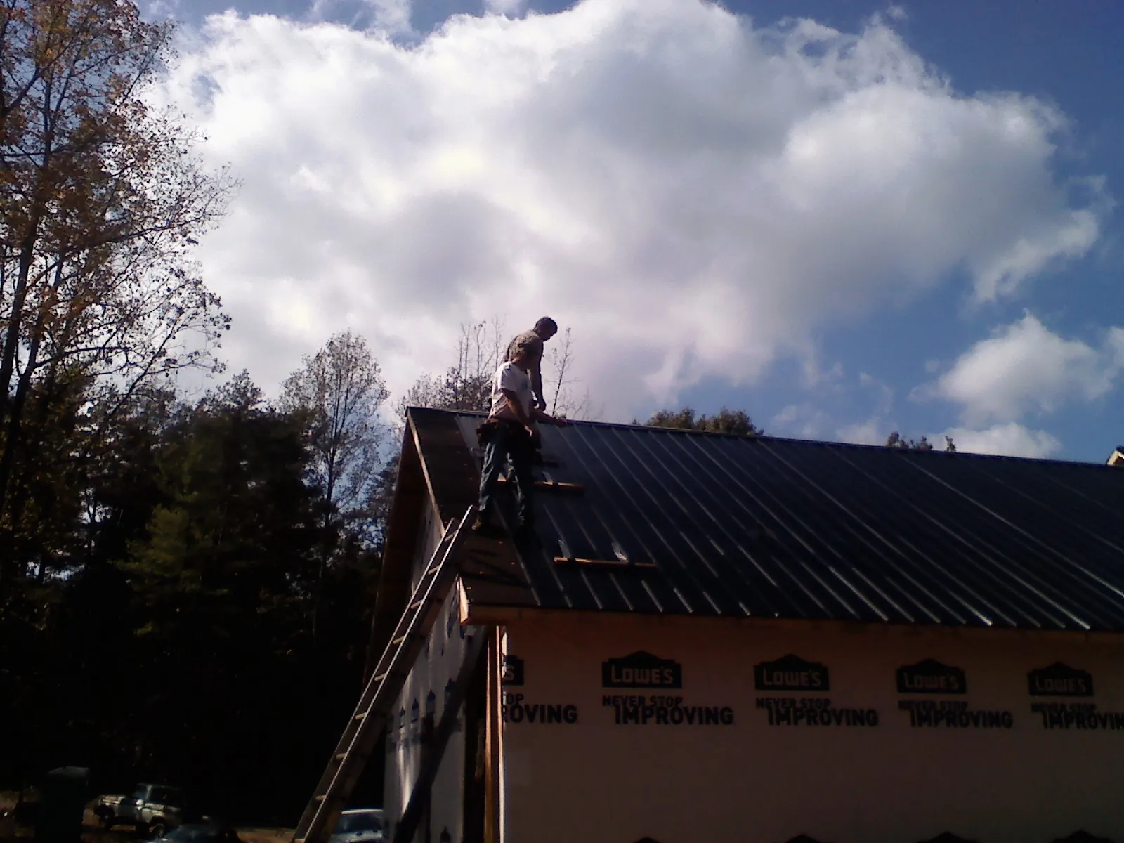 Roofer fastening dark metal panels high against a cloudy sky, from a Roof Inspection job in Montchanin