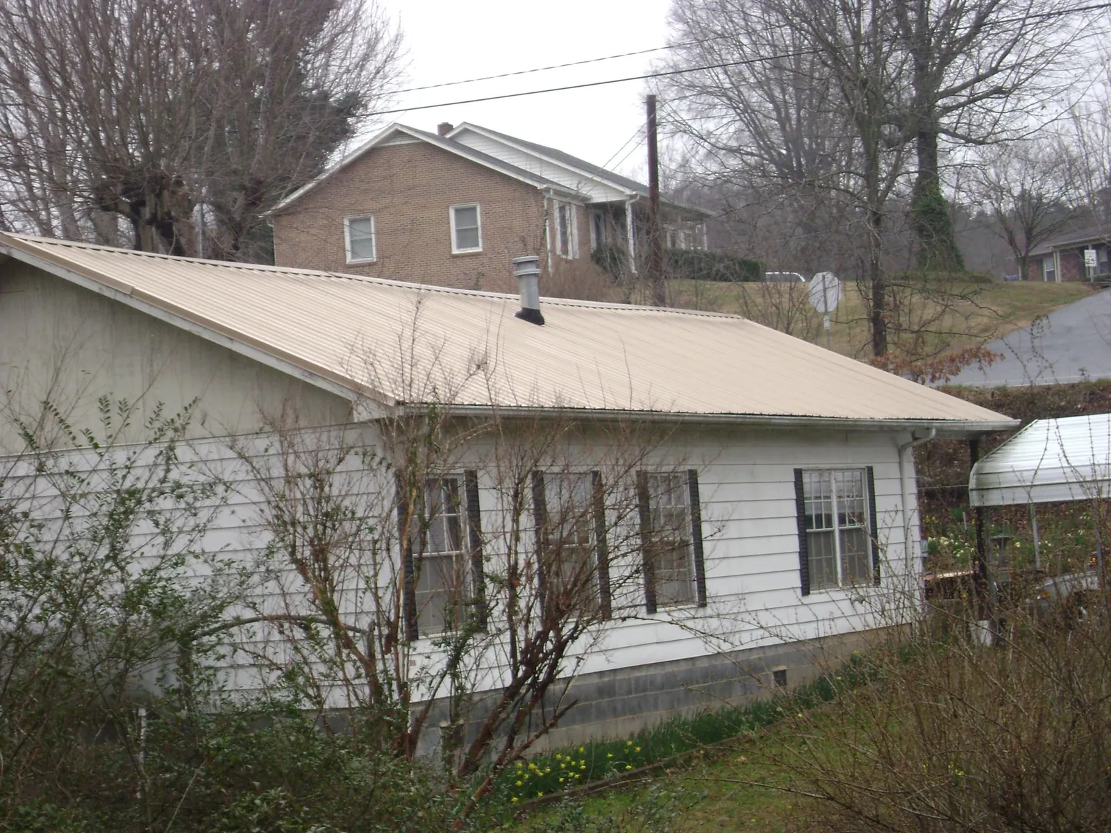 Tan metal roof on a white sided house set into a hillside — Commercial Roofing by Roofing Brothers in Montchanin